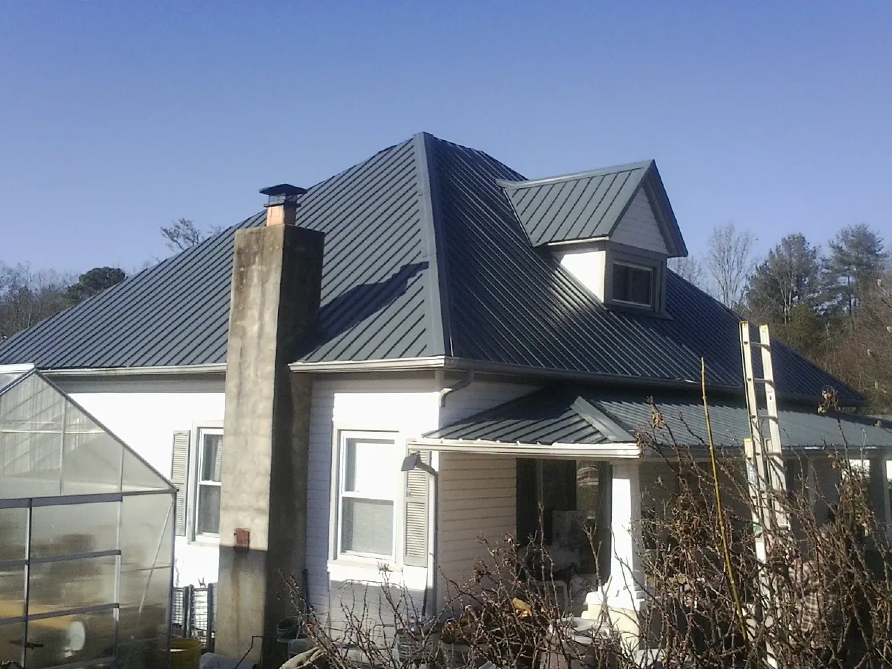 Dark blue standing seam metal roof on a white farmhouse with dormer — Slate & Tile Roof Repair by Roofing Brothers in Boone