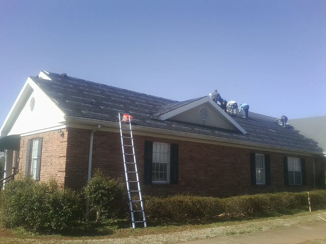 Crew tearing shingles off a brick ranch roof with a ladder set — Metal Roof Repair work by our crew in Boone