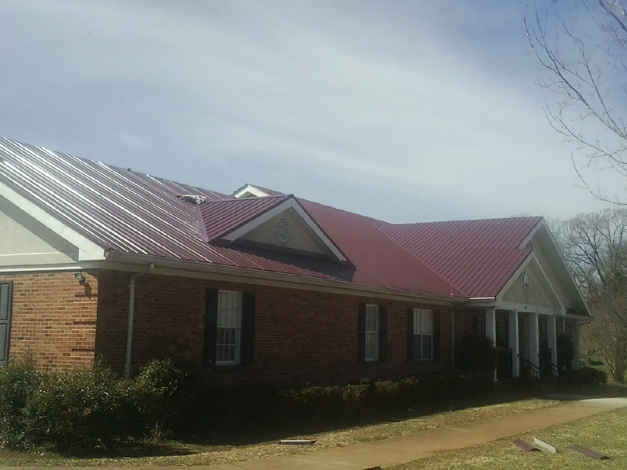 Red metal roof with gabled entries on a long brick building, from a Hail Damage Roof Repair job in Boone
