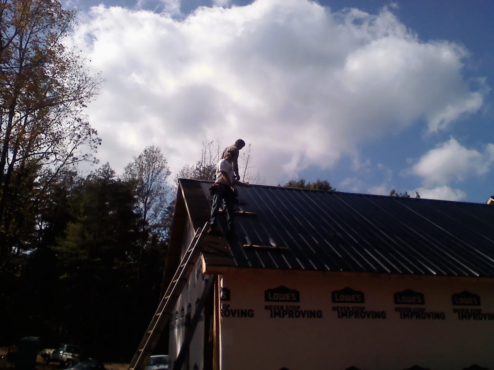 Roofer fastening dark metal panels high against a cloudy sky, from a Roof Inspection job in Boone