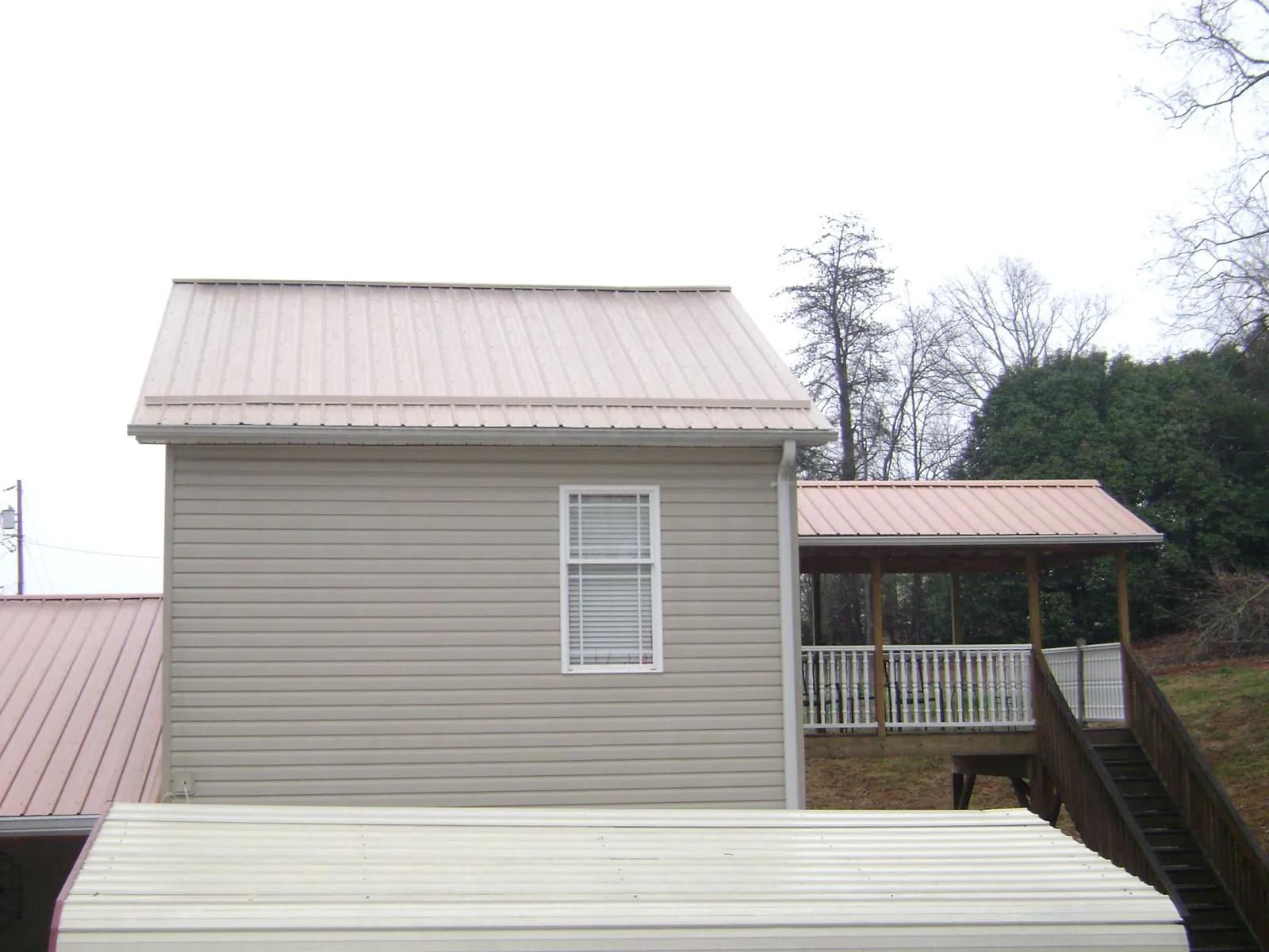 Tan metal roofs on a two story addition and attached porch, from a Roof Replacement job in Boone
